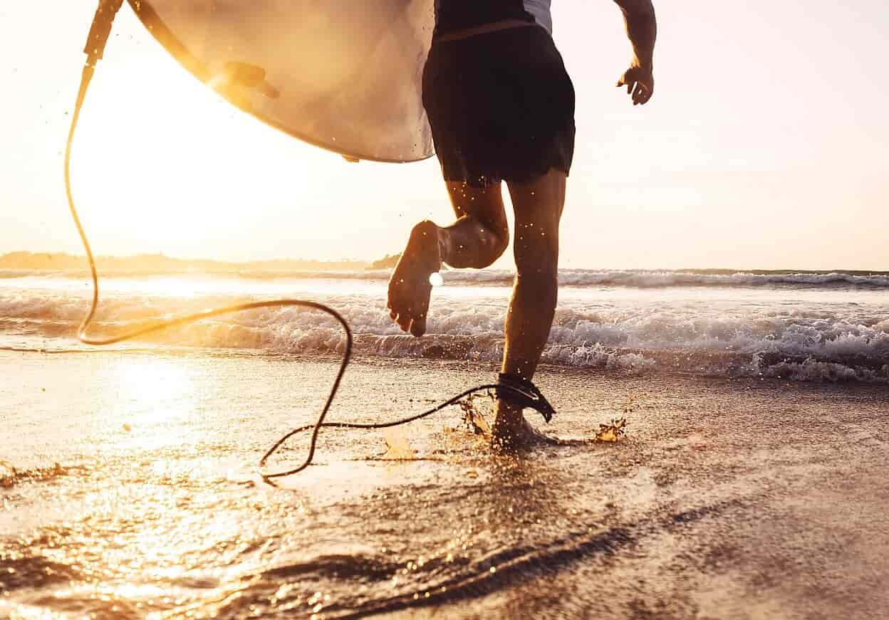 Person running on the beach with a surfboard