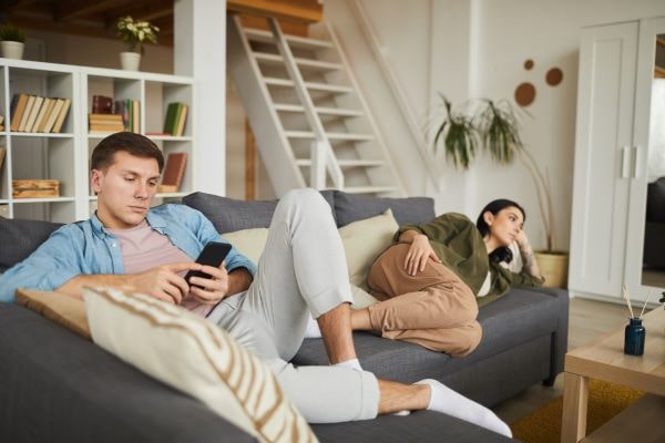 man and woman on couch watching tv looking bored
