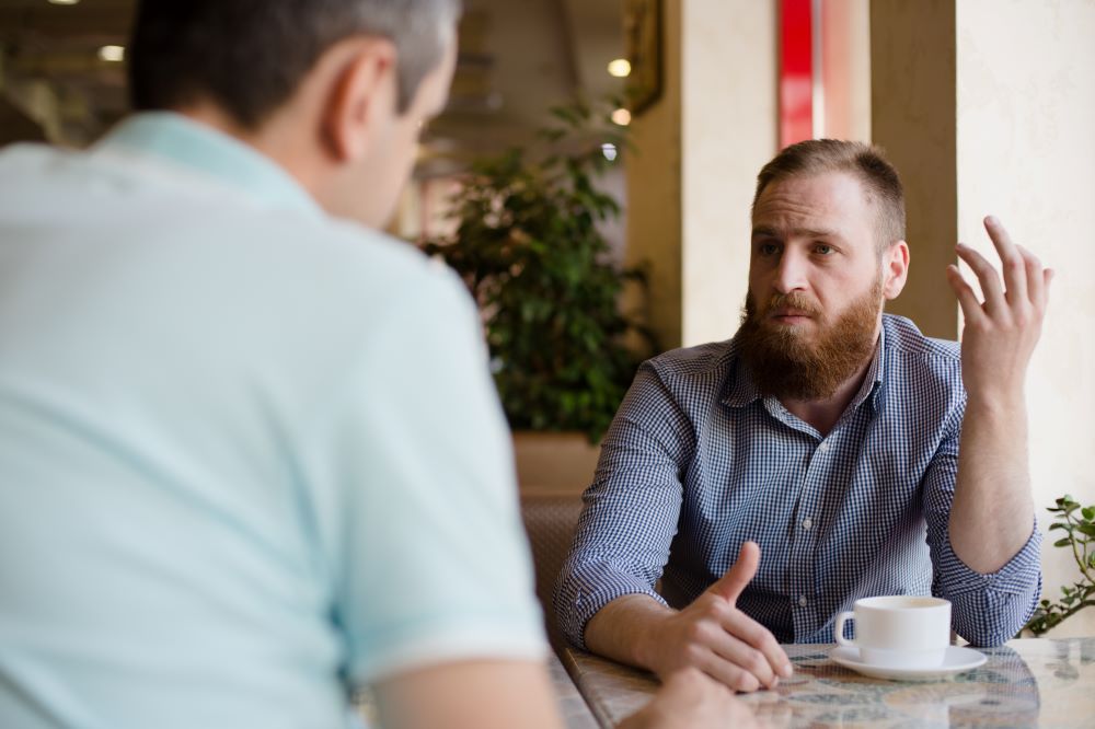 Two men at a table, drinking coffee and having a coaching conversation